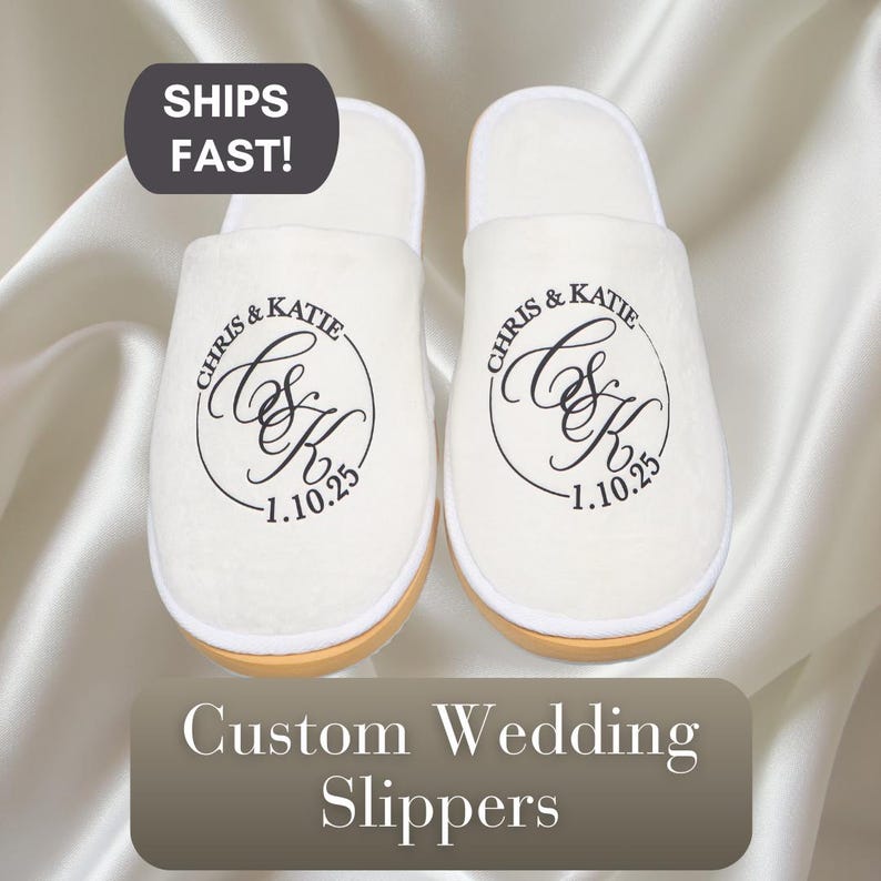 May include: A pair of white slippers with the text "Chris & Katie 1.10.25" embroidered on each slipper. The slippers are a wedding gift for a couple.