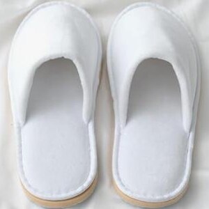 May include: Pair of white hotel slippers with a closed toe and a simple design.
