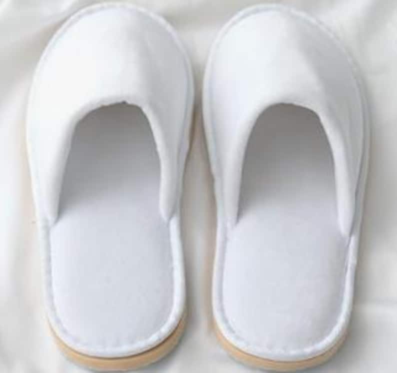 May include: Pair of white hotel slippers with a closed toe and a simple design.