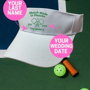 K&ouml;nnte beinhalten: Ein wei&szlig;er Visier mit einem gr&uuml;nen und wei&szlig;en Pickleball-Design. Der Text auf dem Visier lautet "Match Made in Heaven" mit dem Jahr "2024" und "The Smith's". Es gibt rosa Kreise mit dem Text "Your Last Name" und "Your Wedding Date".