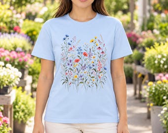 May include: A light blue short-sleeve t-shirt featuring a central graphic print of various colorful wildflowers including red poppies, yellow daisies, and blue cornflowers arranged in a vertical botanical pattern on the front.