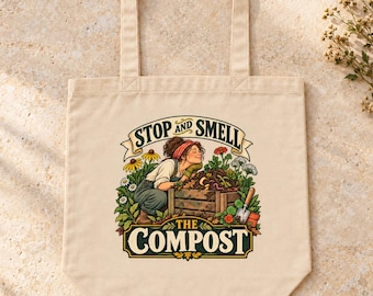 May include: A beige canvas tote bag featuring a colorful graphic of a person kneeling by a wooden compost bin. The text reads STOP AND SMELL THE COMPOST. The illustration includes various flowers, green foliage, and a small garden trowel.