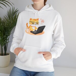Op de afbeelding: Witte hoodie met een cartoonkat die op een laptop werkt. De kat draagt een bril en heeft een kopje koffie en notities in de buurt. De hoodie heeft een voorzak en een capuchon met trekkoord.