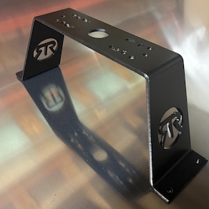 May include: A black metal bracket with a curved top and two vertical sides. The bracket has several holes and a circular cutout with a logo on each side. The bracket is designed to mount equipment.