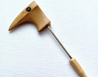 May include: A wooden bird-shaped pin with a brown eye and a wooden handle. The pin is attached to a metal rod.