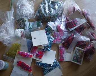 May include: Assortment of colorful sequins and beads in plastic bags. The bags are labeled with handwritten notes.  The sequins are in various colors, including red, blue, green, and pink.  The beads are in various shapes and sizes.