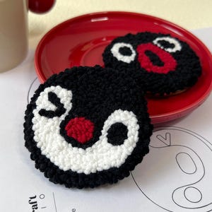 May include: Two black and white felt circle ornaments with red accents, resembling a cartoon face. The ornaments are on a red plate.