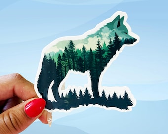 May include: A die-cut sticker showing a wolf silhouette filled with a forest scene. The wolf is in dark green and black, with evergreen trees inside. The background is a gradient of blue hues, with a white border.