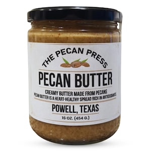 May include: A jar of pecan butter with a black lid and a white label. The label reads "THE PECAN PRESS PECAN BUTTER" with text below stating "CREAMY BUTTER MADE FROM PECANS" and "POWELL, TEXAS". The jar contains 16 oz. (454 g.) of pecan butter.