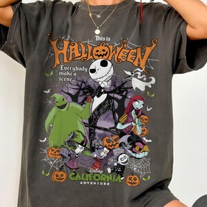 May include: Pepper-colored t-shirt featuring a graphic of Jack Skellington, Sally, and Oogie Boogie from The Nightmare Before Christmas. The shirt has the text "This is Halloween" and "Disney California Adventure".