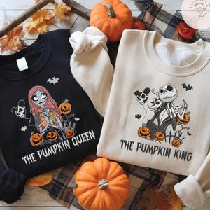 May include: A black sweatshirt featuring a graphic of a female character with long red hair and the text THE PUMPKIN QUEEN, and a cream sweatshirt featuring a graphic of a skeleton character and the text THE PUMPKIN KING, both with pumpkins.