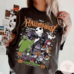 May include: Dark gray t-shirt featuring a graphic from "The Nightmare Before Christmas." The design includes Jack Skellington, Sally, Oogie Boogie, and other characters, with the text "This is Halloween" and "California Adventure."