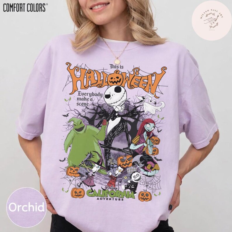 May include: Orchid-colored t-shirt with a graphic featuring characters from The Nightmare Before Christmas. The design includes Jack Skellington, Sally, and Oogie Boogie, with the text "This is Halloween" and "California Adventure."