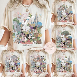 Puede incluir: Camisetas color crema con gr&aacute;ficos coloridos de personajes de Disney. Las camisetas muestran varios nombres de parques de Disney, incluyendo "Magic Kingdom" y "Hollywood Studios". Los dise&ntilde;os incluyen Mickey Mouse, Minnie Mouse y otros personajes queridos.