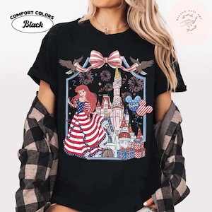 May include: Black Comfort Colors t-shirt with a patriotic design. The graphic includes a princess in a red, white, and blue dress, a castle, fireworks, and a Mickey Mouse balloon. The shirt also has the text "Name".