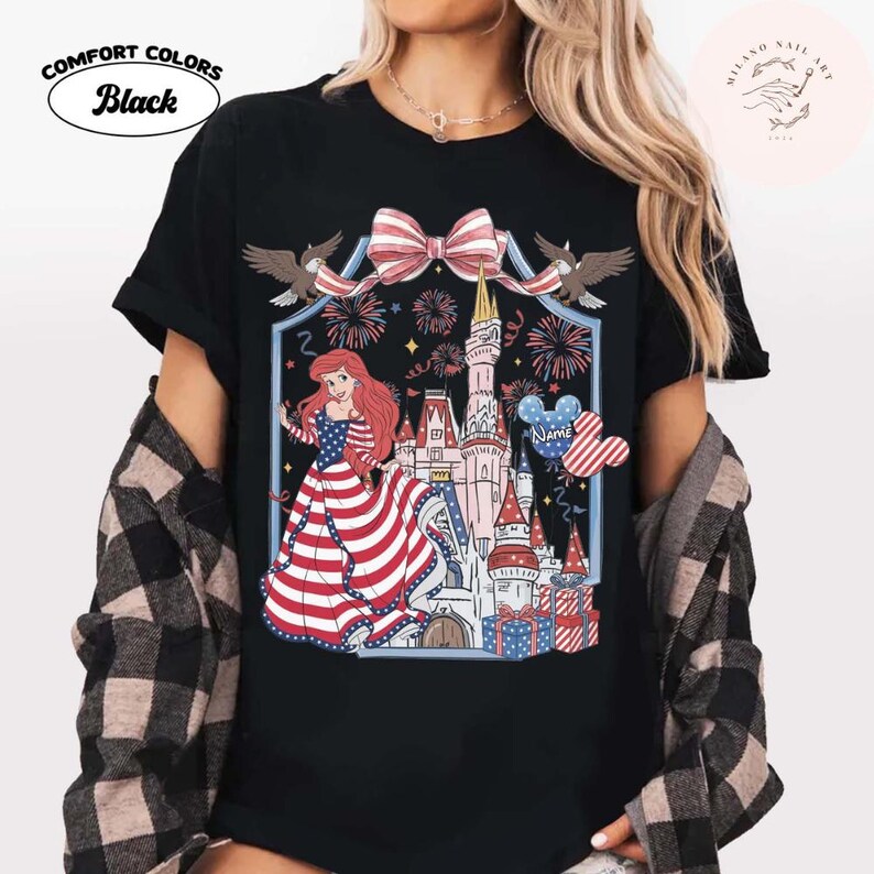 May include: Black Comfort Colors t-shirt with a patriotic design. The graphic includes a princess in a red, white, and blue dress, a castle, fireworks, and a Mickey Mouse balloon. The shirt also has the text "Name".