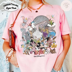Puede incluir: Camiseta rosa claro Comfort Colors con un gr&aacute;fico colorido de personajes de Disney y el logotipo de Epcot. El dise&ntilde;o incluye a Mickey Mouse, Minnie Mouse y otros personajes. La camiseta tiene la inscripci&oacute;n "Light Pink".