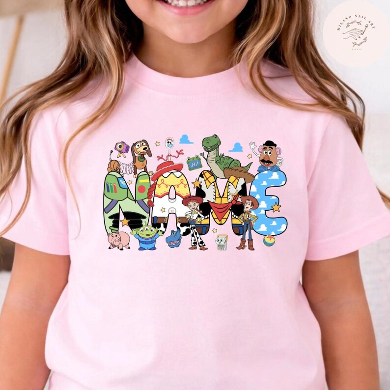 以下が含まれることがあります： NAMEという文字が大きくプリントされたライトピンクのTシャツ。各文字はトイ・ストーリーのキャラクターにインスパイアされた模様や色で装飾されており、映画のキャストの小さなイラストが周囲に散りばめられています。
