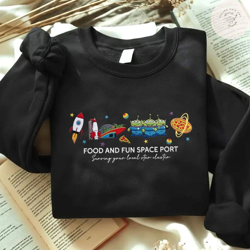 May include: Black sweatshirt with a colorful graphic featuring a rocket, pizza, and three green aliens. The text "FOOD AND FUN SPACE PORT" and "Serving your local star cluster" are printed below the graphic.