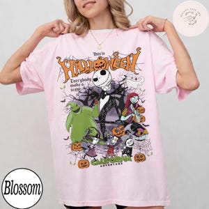 May include: A light pink t-shirt featuring a graphic design with characters from The Nightmare Before Christmas. The design includes the text "This is Halloween" and "Everybody make a scene". The shirt also has the text "Disney California Adventure".