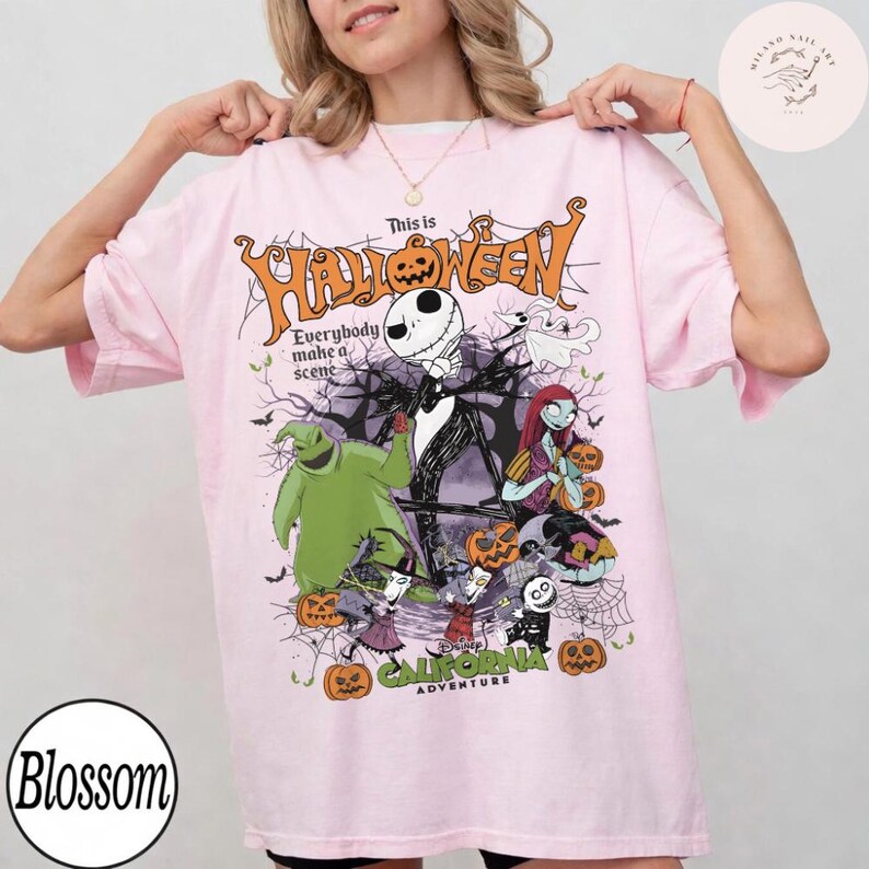 May include: A light pink t-shirt featuring a graphic design with characters from The Nightmare Before Christmas. The design includes the text "This is Halloween" and "Everybody make a scene". The shirt also has the text "Disney California Adventure".