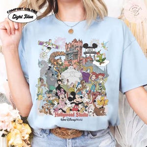 Puede incluir: Camiseta Comfort Colors azul claro con un gr&aacute;fico colorido de personajes de Disney y atracciones de Hollywood Studio. El dise&ntilde;o incluye a Mickey Mouse, Minnie Mouse, Buzz Lightyear y el Hollywood Tower Hotel. El texto en la camiseta dice "Hollywood Studio Walt Disney World."
