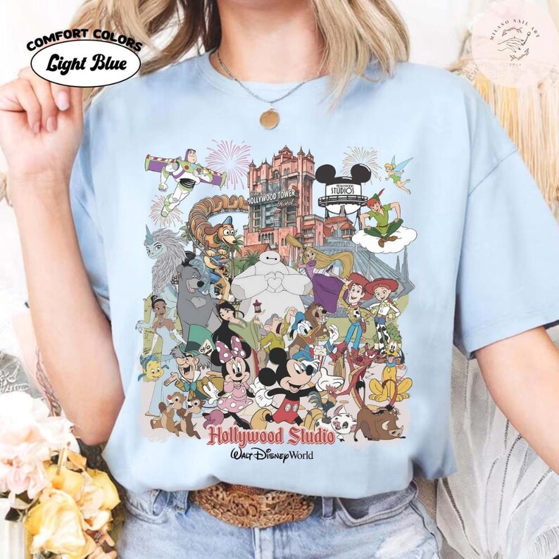 Puede incluir: Camiseta Comfort Colors azul claro con un gr&aacute;fico colorido de personajes de Disney y atracciones de Hollywood Studio. El dise&ntilde;o incluye a Mickey Mouse, Minnie Mouse, Buzz Lightyear y el Hollywood Tower Hotel. El texto en la camiseta dice "Hollywood Studio Walt Disney World."