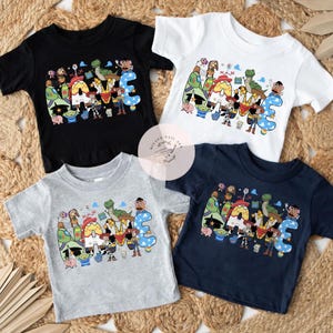 以下が含まれることがあります： 黒、白、グレー、ネイビーの半袖Tシャツ4枚。各シャツには、ウッディ、バズ、レックスなど、トイ・ストーリーのカラフルなキャラクターで綴られた「NAME」という文字のグラフィックプリントが施されています。