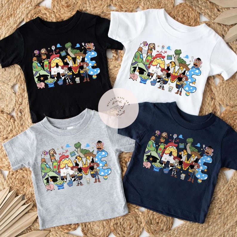 以下が含まれることがあります： 黒、白、グレー、ネイビーの半袖Tシャツ4枚。各シャツには、ウッディ、バズ、レックスなど、トイ・ストーリーのカラフルなキャラクターで綴られた「NAME」という文字のグラフィックプリントが施されています。