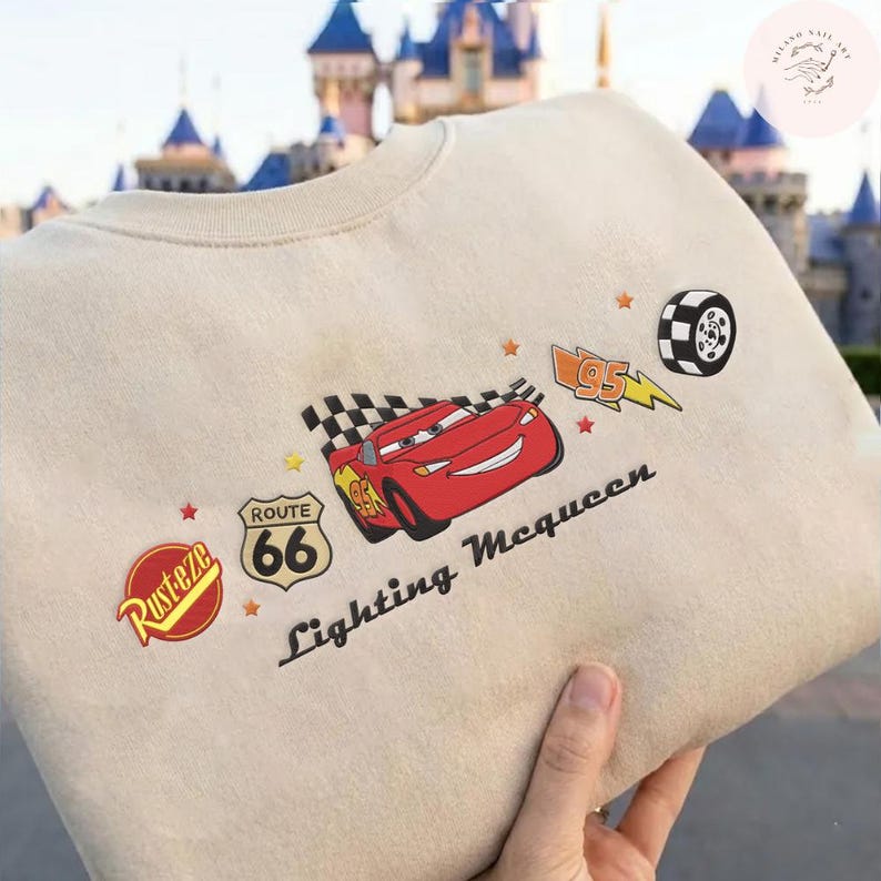 May include: Beige crew neck sweatshirt with a red Lightning McQueen graphic and the text "Lightning McQueen". The design includes a checkered flag, Route 66 logo, and a tyre. The sweatshirt has a classic, casual style.