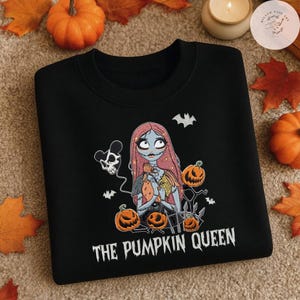 May include: A black crewneck sweatshirt featuring a graphic print of a female character with long pink hair, surrounded by orange jack-o'-lanterns, bats, and a skull-shaped balloon. The text "THE PUMPKIN QUEEN" is printed in white below the graphic.