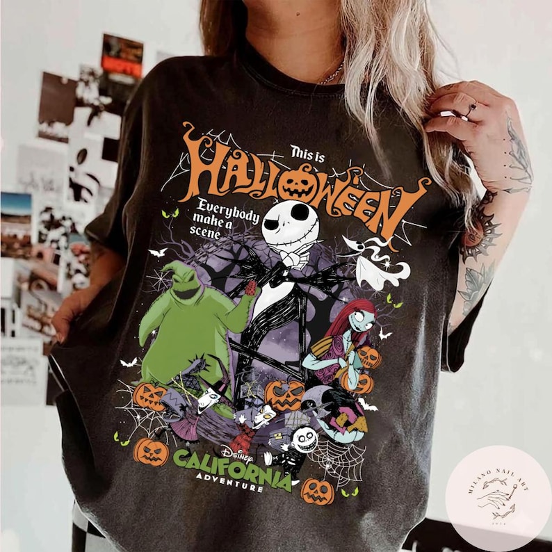 May include: Dark gray t-shirt featuring a graphic from "The Nightmare Before Christmas." The design includes Jack Skellington, Sally, Oogie Boogie, and other characters, with the text "This is Halloween" and "California Adventure."