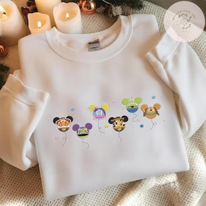 May include: White crewneck sweatshirt featuring embroidered cartoon character balloons in various colors. The balloons have character faces and are decorated with stars and other small details. The sweatshirt is a cozy, casual style.