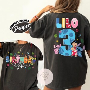 May include: Dark gray t-shirt with colorful graphics featuring the characters Lilo and Stitch. The back of the shirt displays the word "Lilo", the number "3", and the characters. The front of the shirt says "Birthday girl".