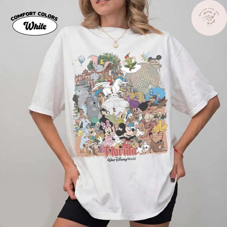 Puede incluir: Camiseta blanca con un gr&aacute;fico colorido que presenta varios personajes de Disney y el texto "Florida Walt Disney World". La camiseta tiene las palabras "Comfort Colors White" en un dise&ntilde;o circular.