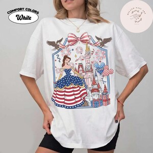 May include: White Comfort Colors t-shirt with a patriotic graphic featuring a princess in a dress with stars and stripes, a castle, fireworks, and a bow. The shirt has the word "White" on it.