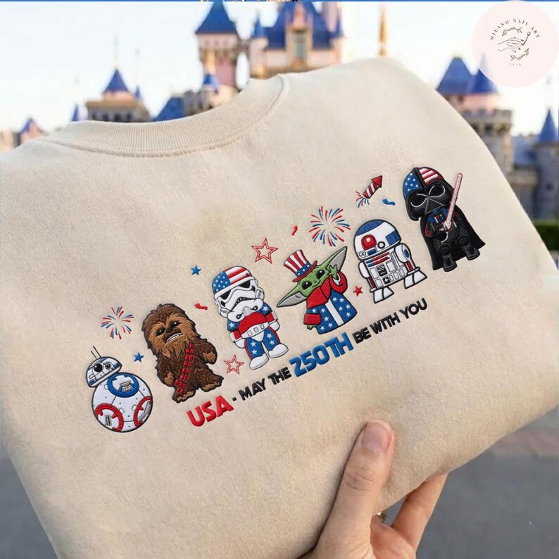 Op de afbeelding: Beige sweatshirt met Star Wars-personages in patriottische kleding. Het ontwerp bevat Chewbacca, een Stormtrooper en Darth Vader, met de tekst "USA - MAY THE 250TH BE WITH YOU."