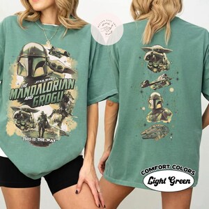 May include: Light green t-shirt with graphics from the Star Wars series, "The Mandalorian and Grogu." The front shows the Mandalorian helmet, Grogu, and spacecraft. The back has more character and spacecraft graphics. The text "This is the Way" is also visible. The shirt is labelled "Comfort Colors Light Green."