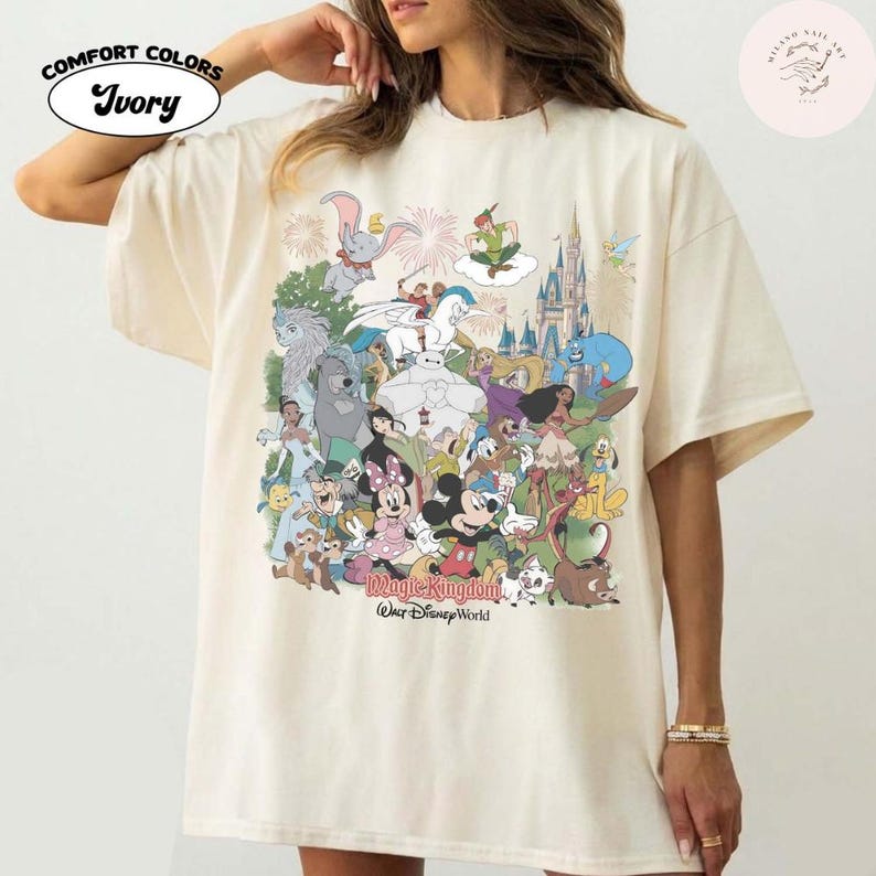 Puede incluir: Camiseta Comfort Colors color marfil con un gr&aacute;fico colorido de varios personajes de Disney, incluyendo Mickey y Minnie Mouse, Dumbo y Peter Pan. Las palabras "Magic Kingdom" y "Our Disney World" est&aacute;n impresas en la camiseta.