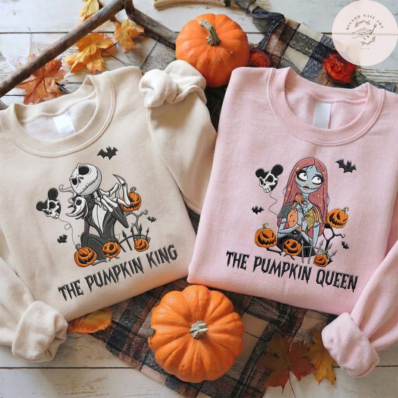 May include: A beige sweatshirt featuring a graphic of a skeleton character and the text THE PUMPKIN KING, and a light pink sweatshirt featuring a graphic of a female skeleton character and the text THE PUMPKIN QUEEN, both with pumpkins.