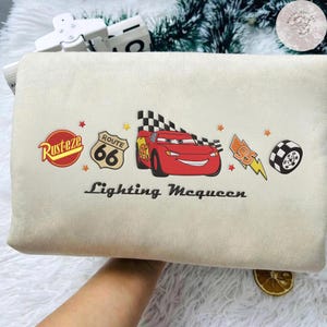 May include: Beige rectangular cushion featuring a red Lightning McQueen race car design with the text "Lightning McQueen". Other graphics include Route 66, a checkered flag, and the word "Rusteze".