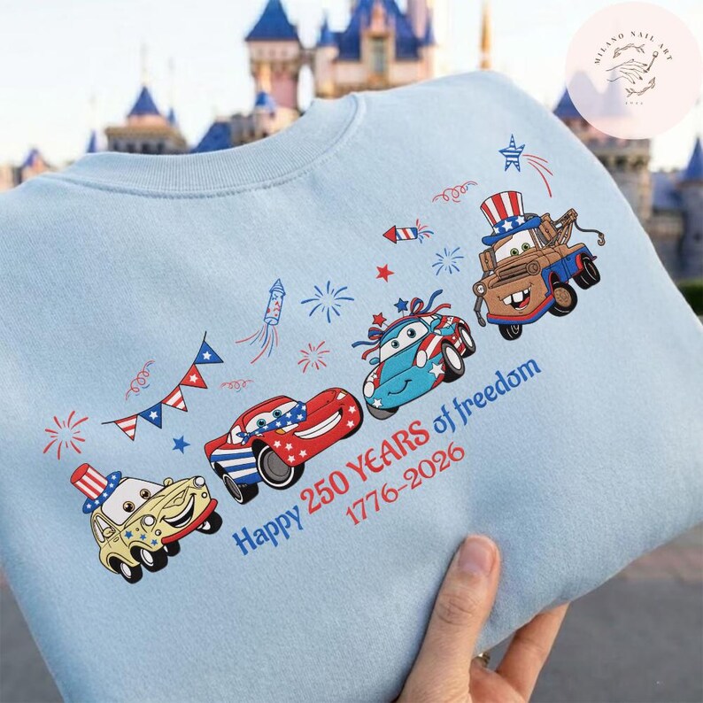 Pode incluir: Camisola azul clara com carros de desenho animado decorados com temas patri&oacute;ticos. O design inclui fogos de artif&iacute;cio, estrelas e o texto "Happy 250 Years of freedom 1776-2026". Os carros s&atilde;o vermelhos, azuis e amarelos.