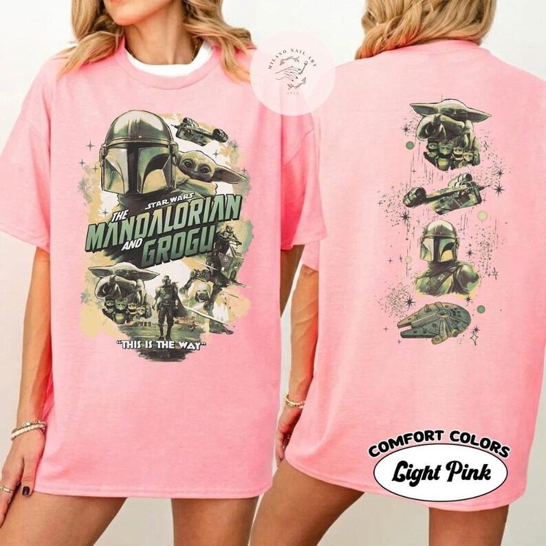 May include: Pale pink t-shirt with a Star Wars theme, showcasing The Mandalorian and Grogu. The front displays "THE MANDALORIAN AND GROGU" and "THIS IS THE WAY". The back features more Star Wars imagery. The shirt is labelled "Comfort Colors Light Pink".
