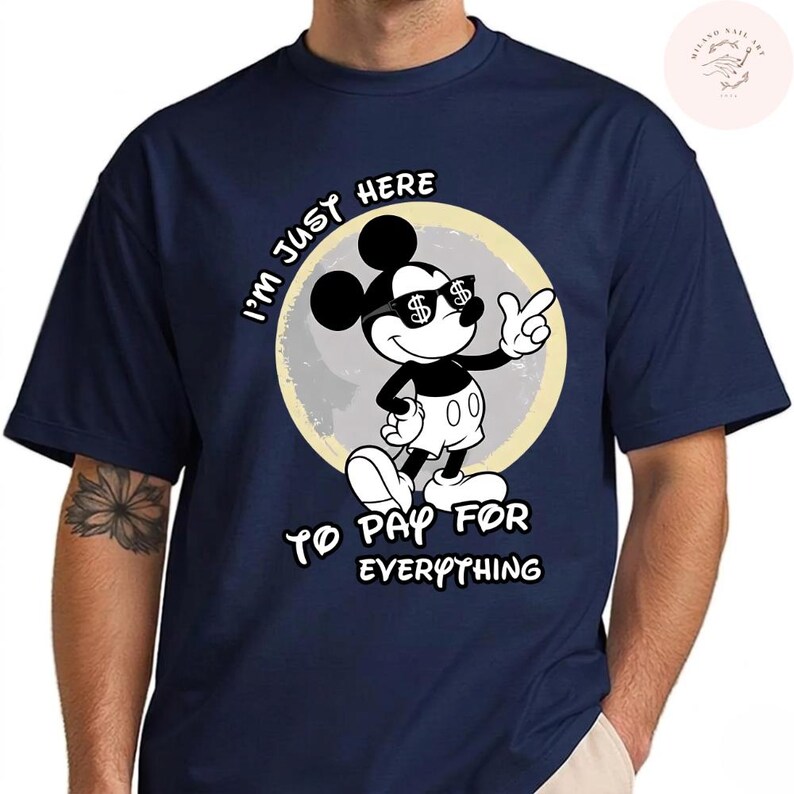 May include: Navy blue t-shirt featuring a cartoon Mickey Mouse character wearing sunglasses with dollar signs. The text reads "I'm just here to pay for everything". The design is set against a light yellow and gray background.