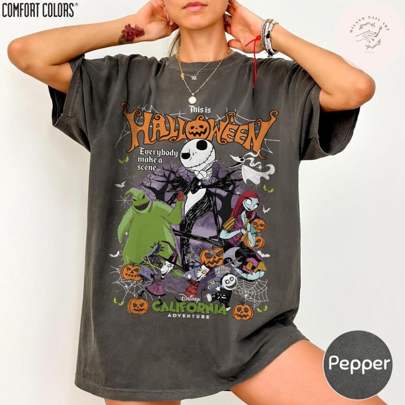 May include: Pepper-colored t-shirt featuring a graphic of Jack Skellington, Sally, and Oogie Boogie from The Nightmare Before Christmas. The shirt has the text "This is Halloween" and "Disney California Adventure".