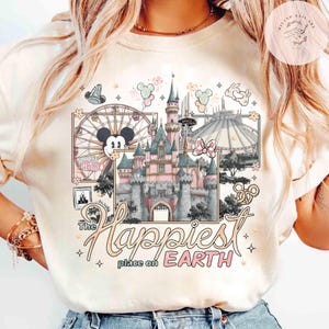 May include: Cream-colored t-shirt featuring a colorful graphic of a Disney castle, Ferris wheel, and Space Mountain. The text "The Happiest Place on Earth" is displayed in a whimsical font. Mickey Mouse and Minnie Mouse are also featured in the design.