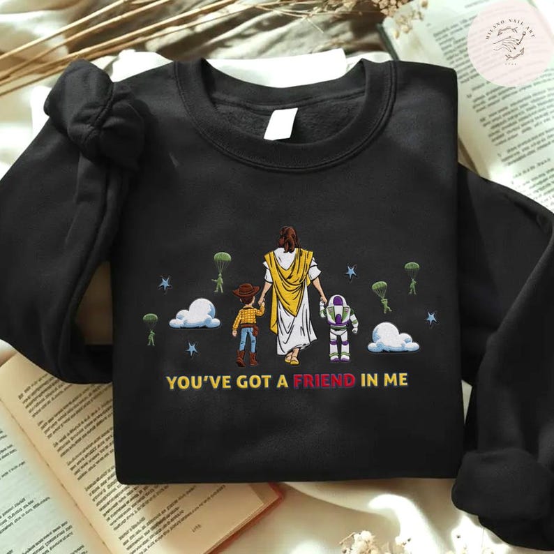 May include: Black sweatshirt with a graphic of Jesus, Woody, and Buzz Lightyear. The design includes clouds, stars, and parachuters. The text "YOU'VE GOT A FRIEND IN ME" is printed at the bottom of the design.