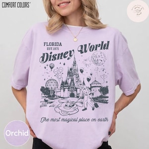 Może przedstawiać: Koszulka w kolorze orchidei z grafiką Disney World. Projekt zawiera zamek, Myszka Miki oraz tekst "Florida Est.1971 Disney World" i "The most magical place on earth". Koszulka jest od Comfort Colors.