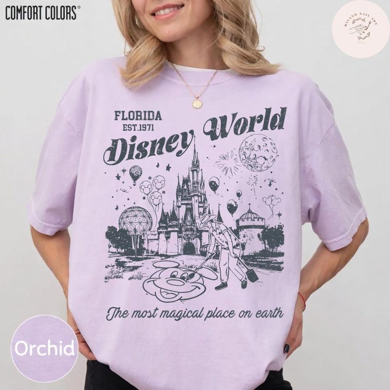 Może przedstawiać: Koszulka w kolorze orchidei z grafiką Disney World. Projekt zawiera zamek, Myszka Miki oraz tekst "Florida Est.1971 Disney World" i "The most magical place on earth". Koszulka jest od Comfort Colors.