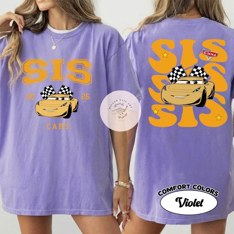 May include: A violet Comfort Colors t-shirt featuring a graphic of a yellow race car with checkered flags. The word "SIS" is printed in gold, along with the number "26" and the word "Cars". The back of the shirt repeats the "SIS" design.